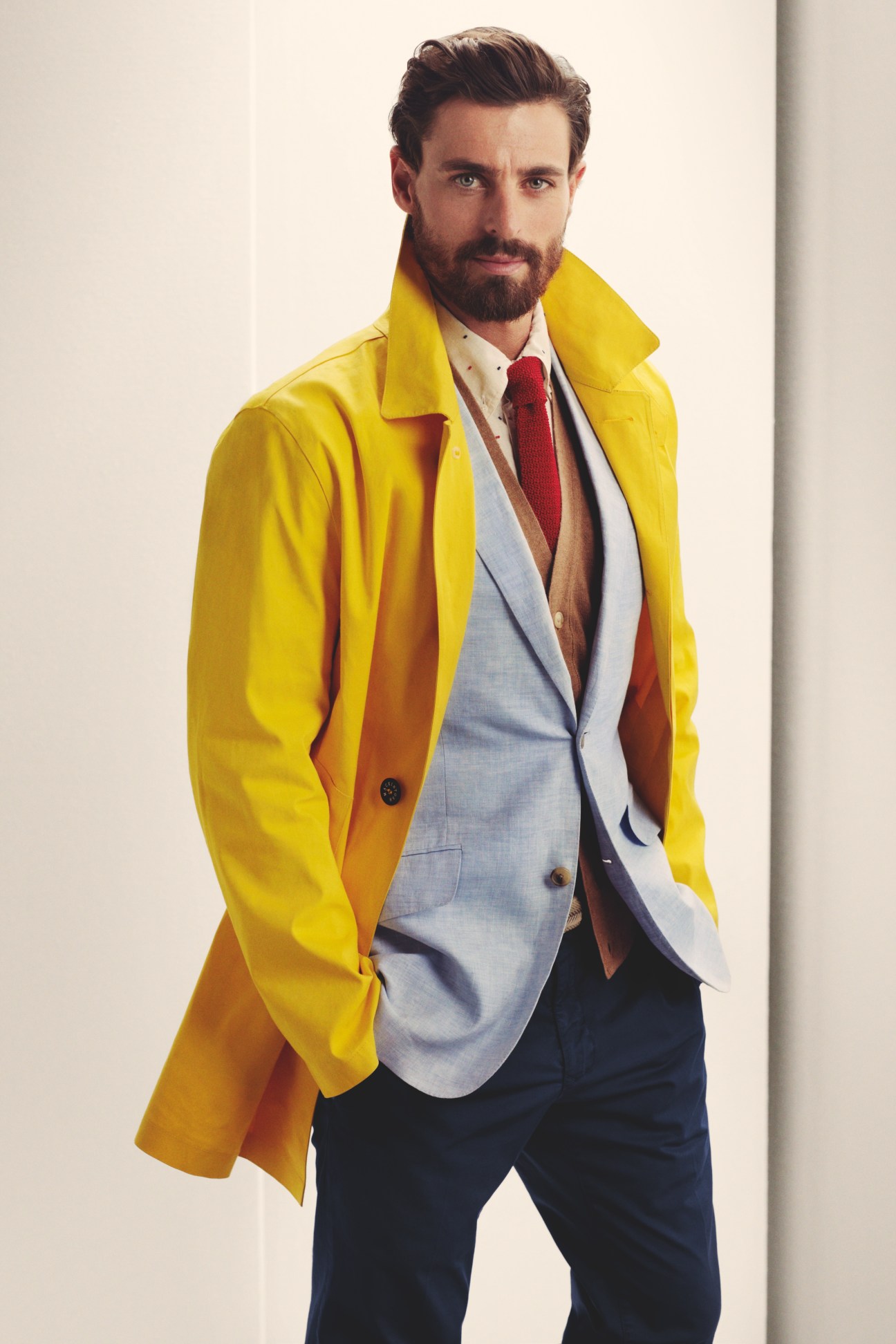Man wearing a bright yellow Mackintosh coat layered over a light blue Richard James jacket with red tie and dark trousers.