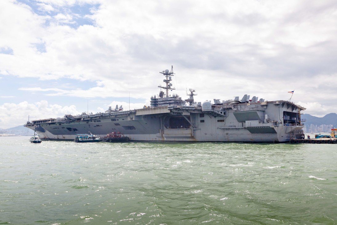 USS George Washington aircraft carrier anchored in Victoria Harbour with Hong Kong skyline in background.