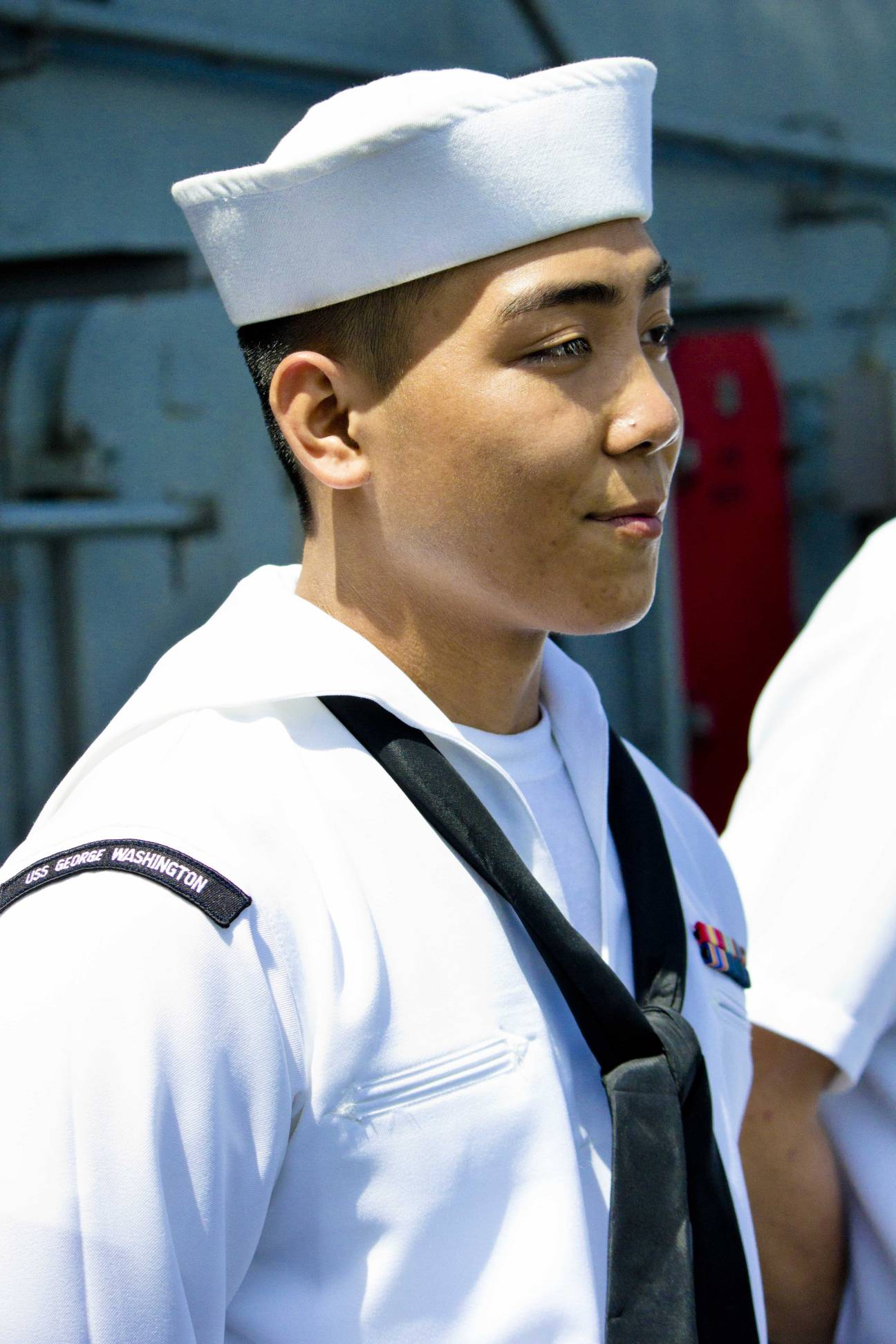 USS George Washington sailor in white Navy uniform and hat standing on flight deck.