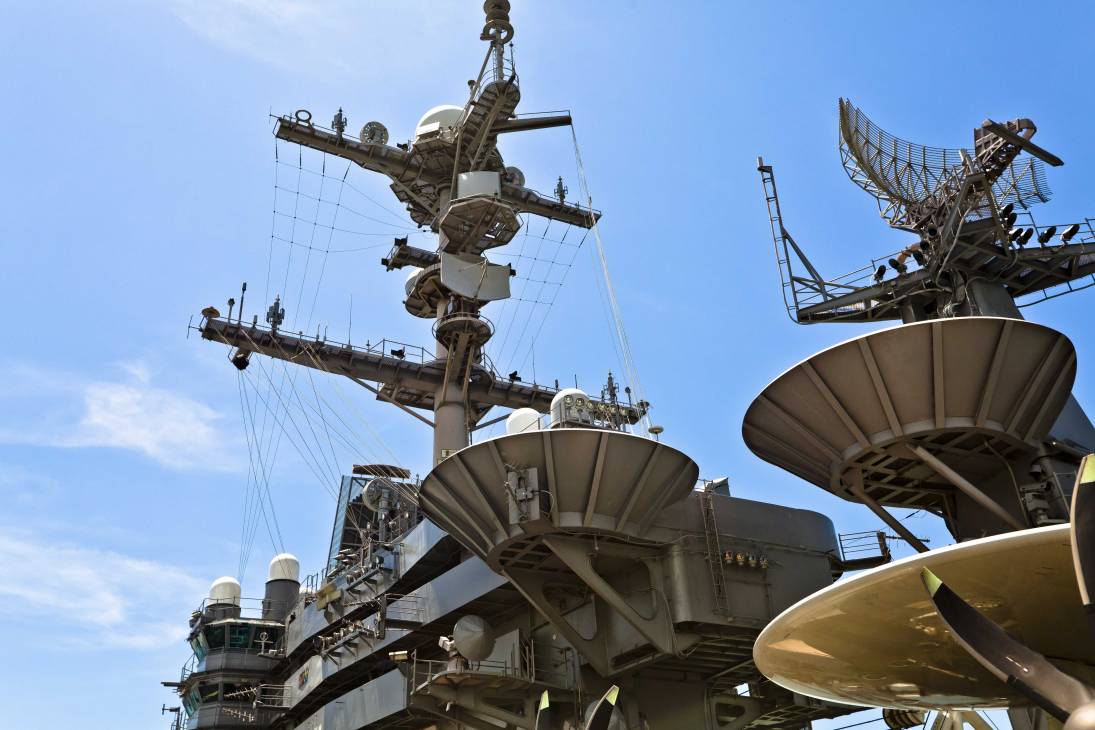 Close-up of USS George Washington's navigation tower showing radar dishes and communication antennas against blue sky.
