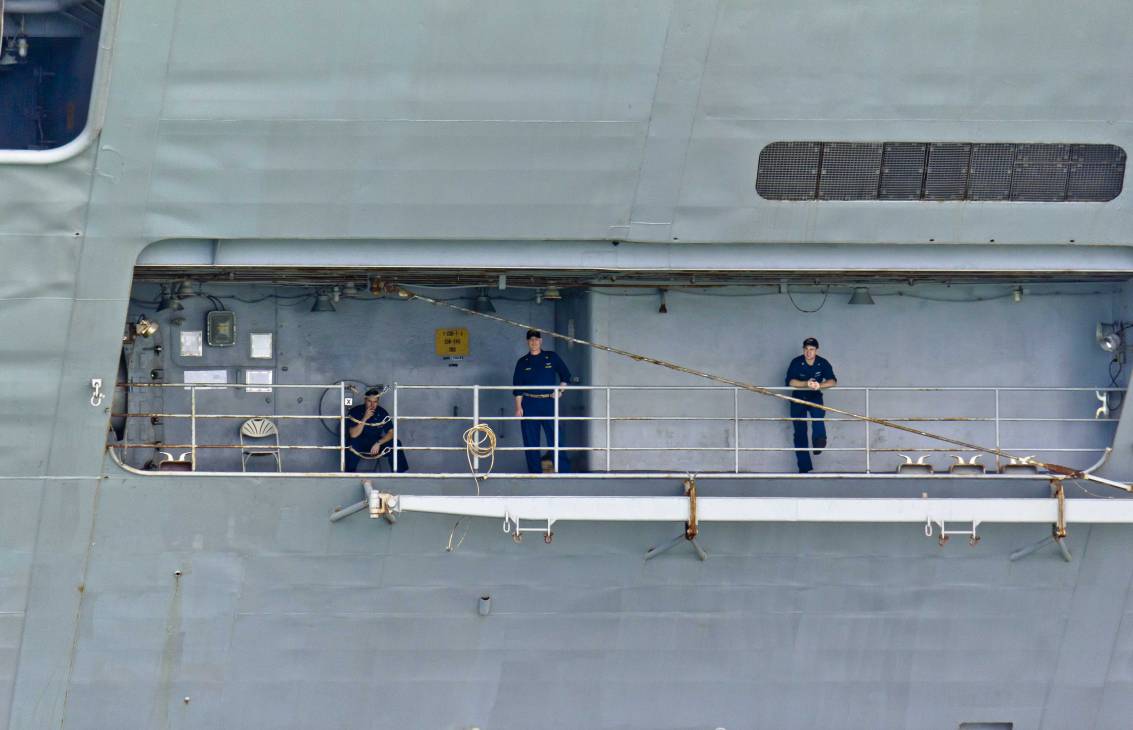 Crew members in navy uniforms stand watch on a deck railing of the USS George Washington aircraft carrier.