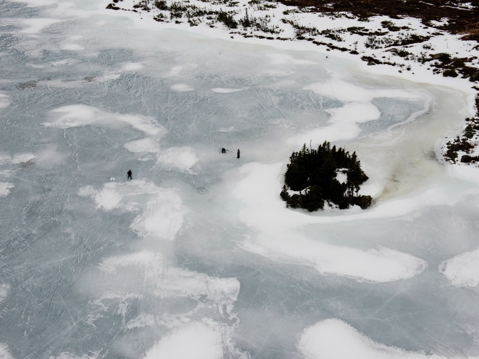 Aerial view of people fishing on a frozen lake with snow and ice patterns visible from above.