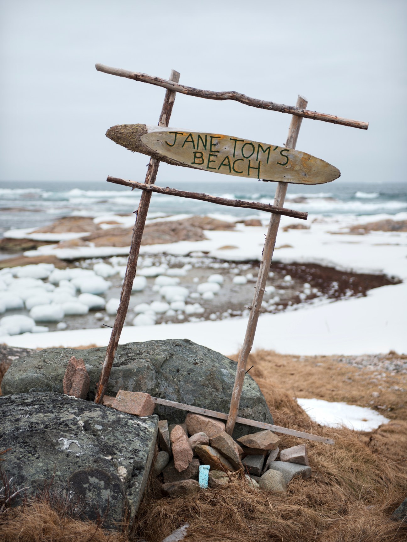 Wooden signpost reading 'JANE TOM'S BEACH' with pack ice and Atlantic Ocean waves in background.