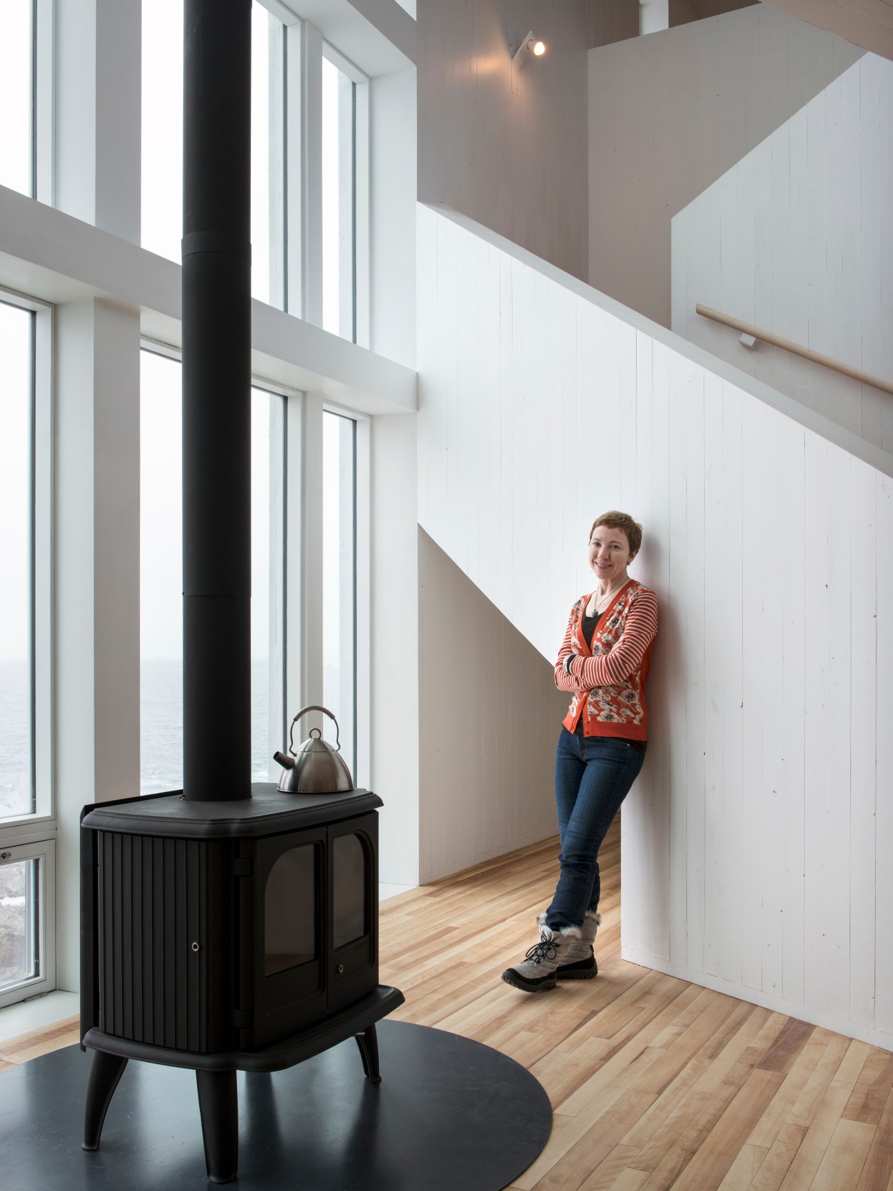 Zita Cobb stands in a modern interior space with high ceilings, large windows, and a black wood stove.