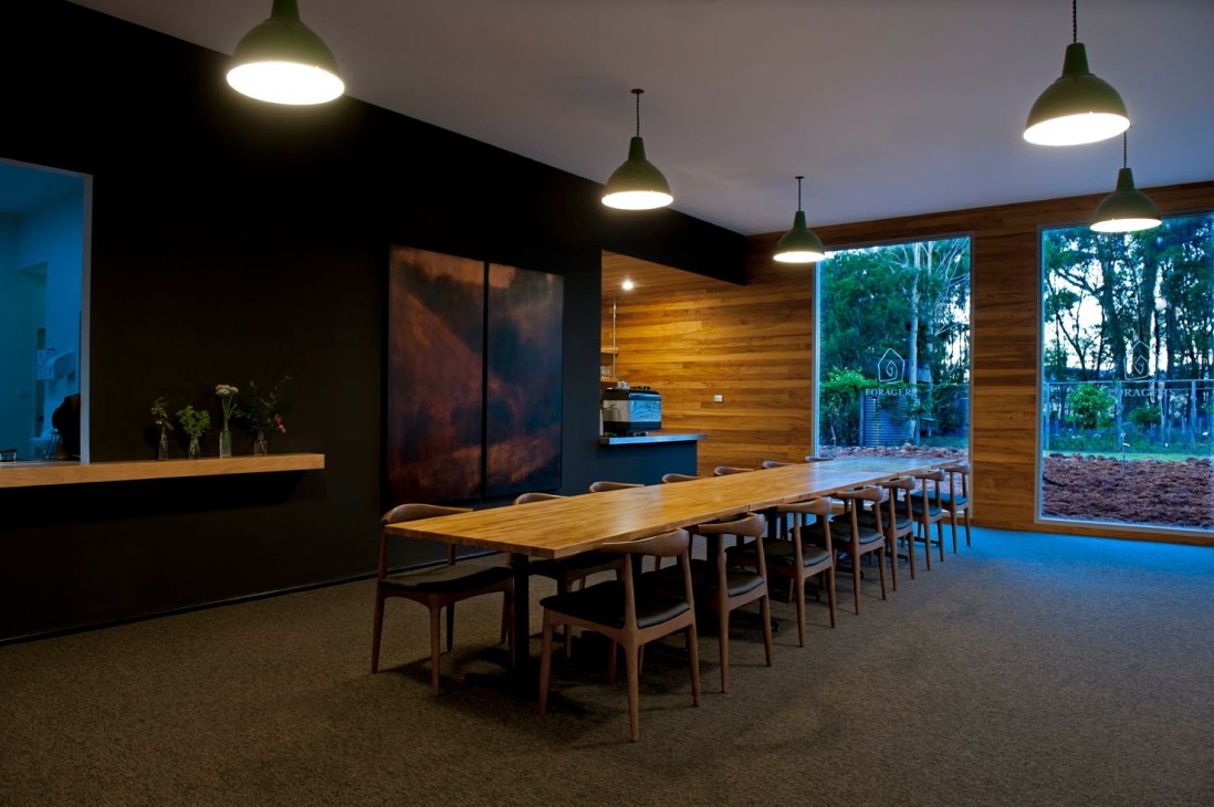 Modern dining space at Foragers cooking school with wooden table, mid-century chairs, pendant lights, and forest views through large windows.