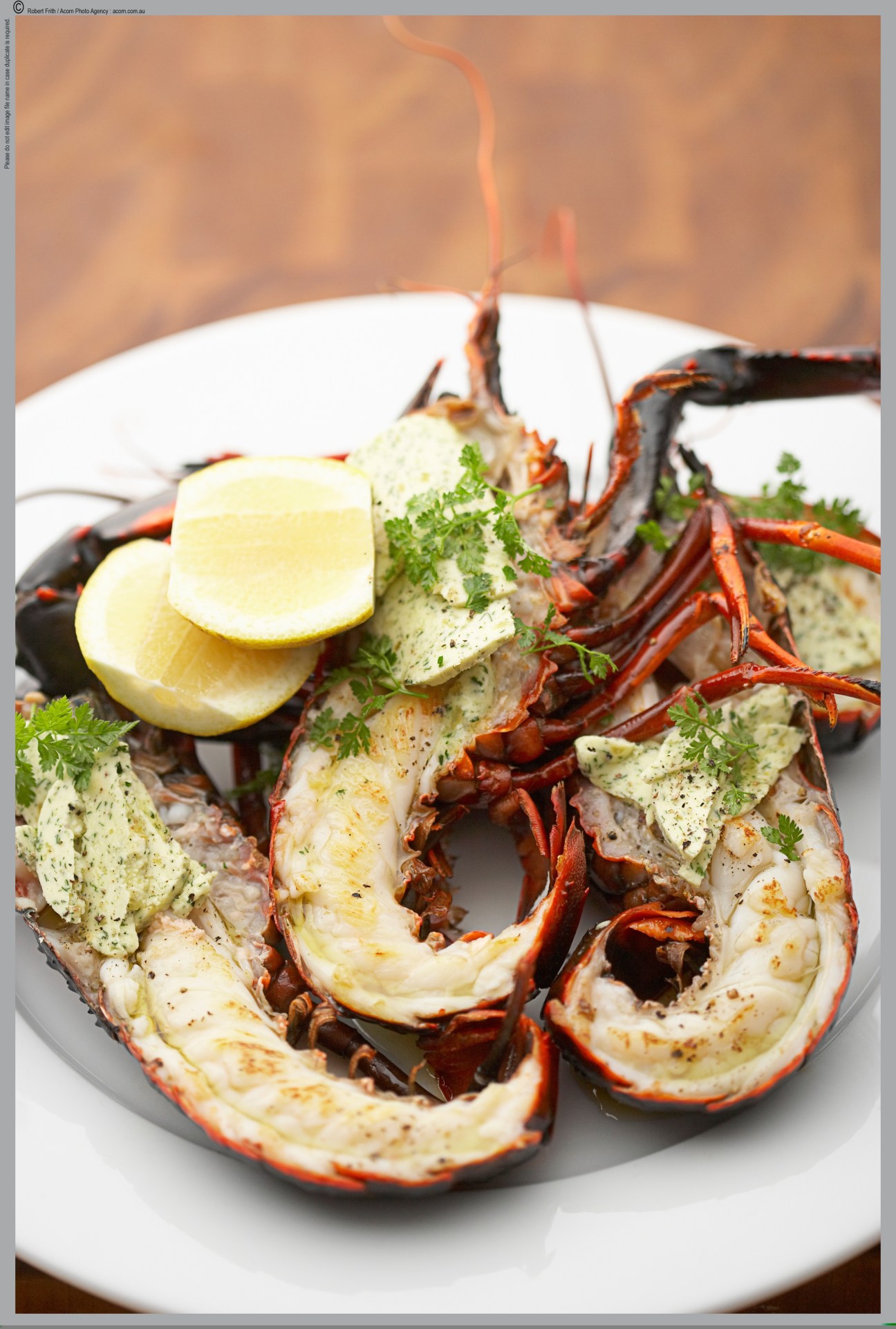 Cooked lobster tails topped with herb butter and lime on a white plate.