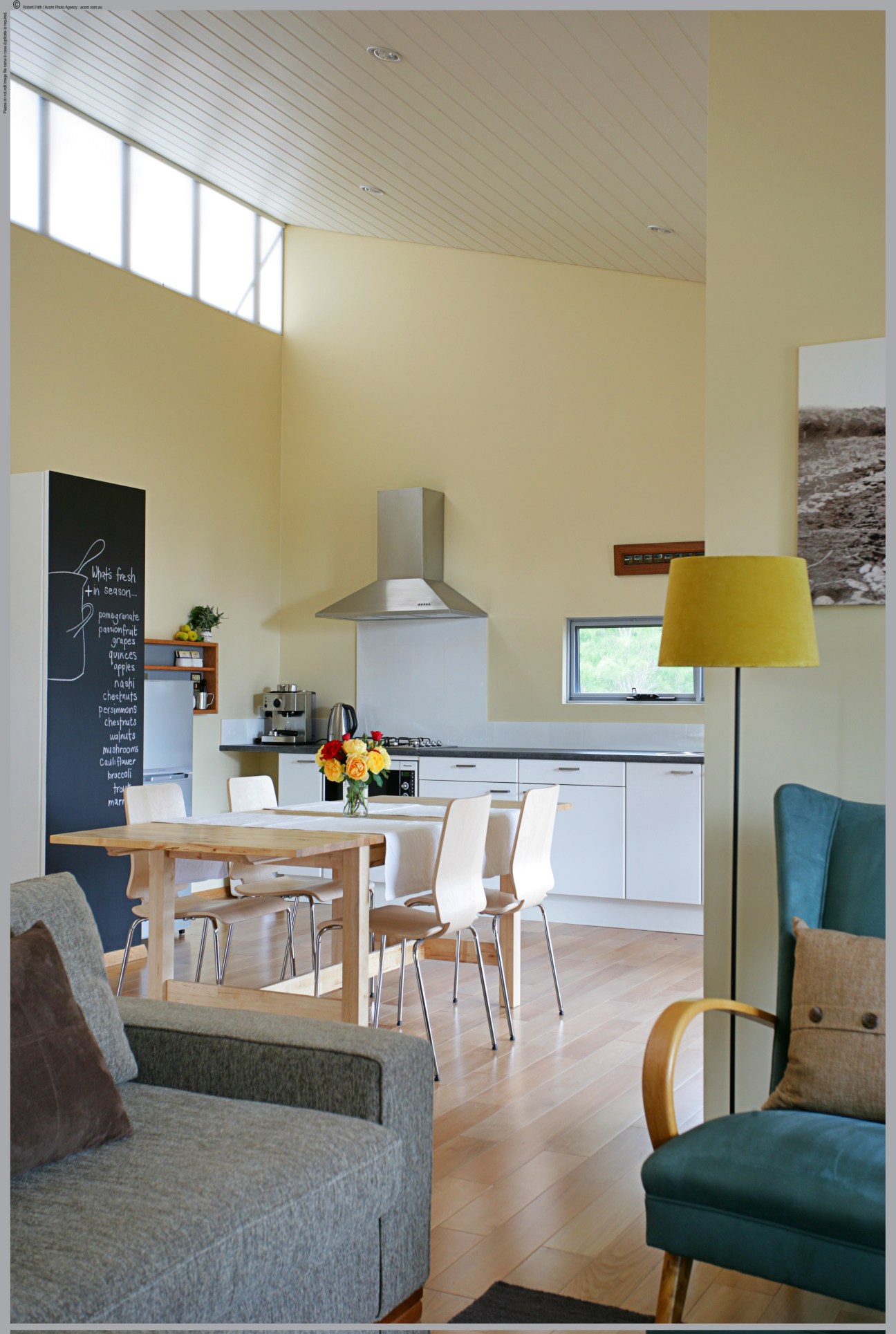 Modern kitchen and dining area with yellow walls, white cabinetry, wooden dining table, and contemporary furnishings.