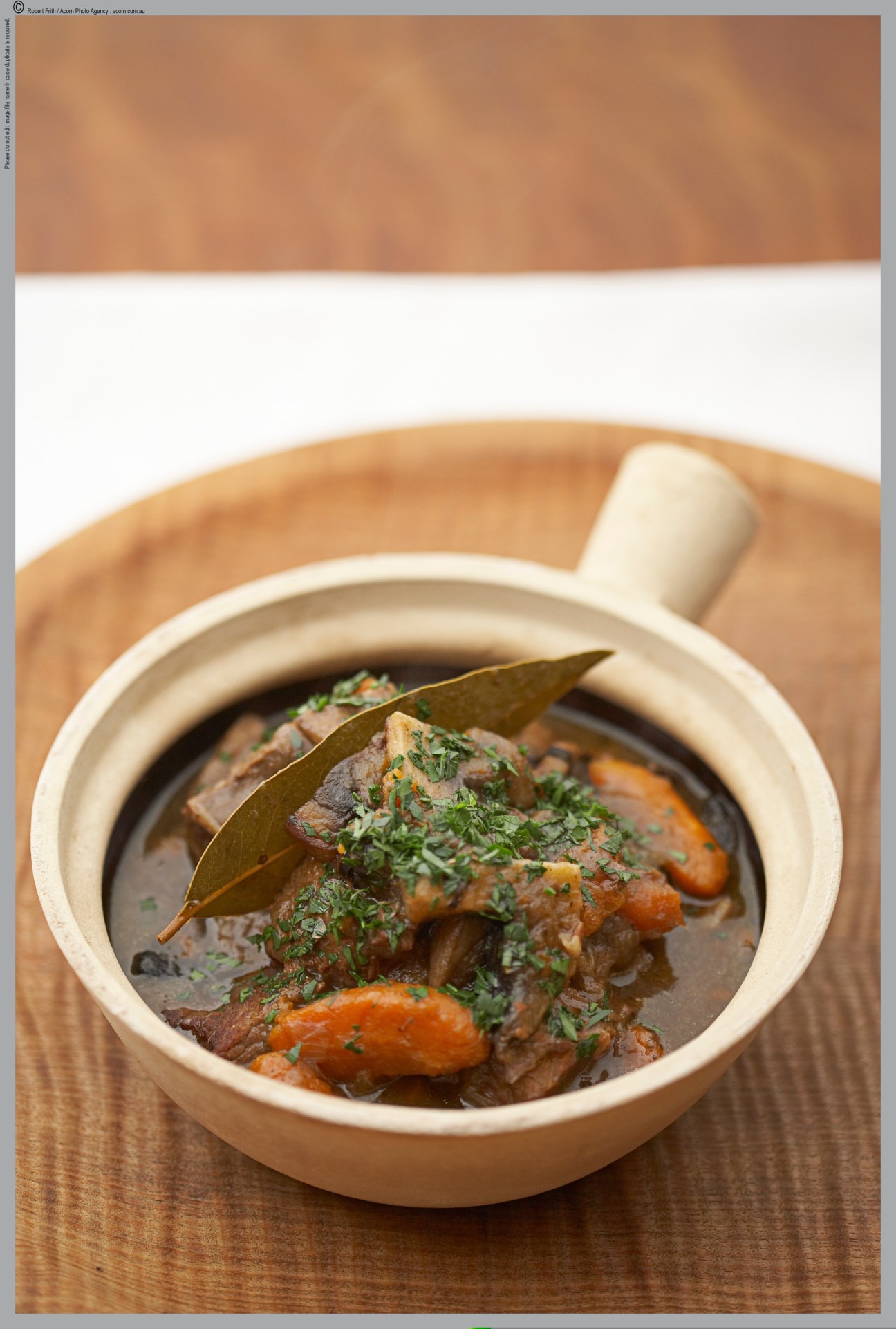 Braised meat with carrots and herbs in a cream-colored bowl with bay leaf garnish.