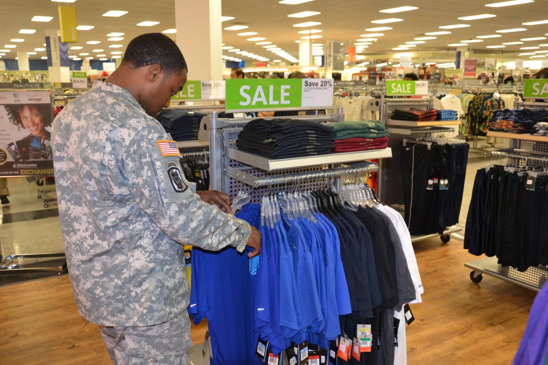 US soldier in camouflage uniform shopping for clothing at a military retail store with sale signs.
