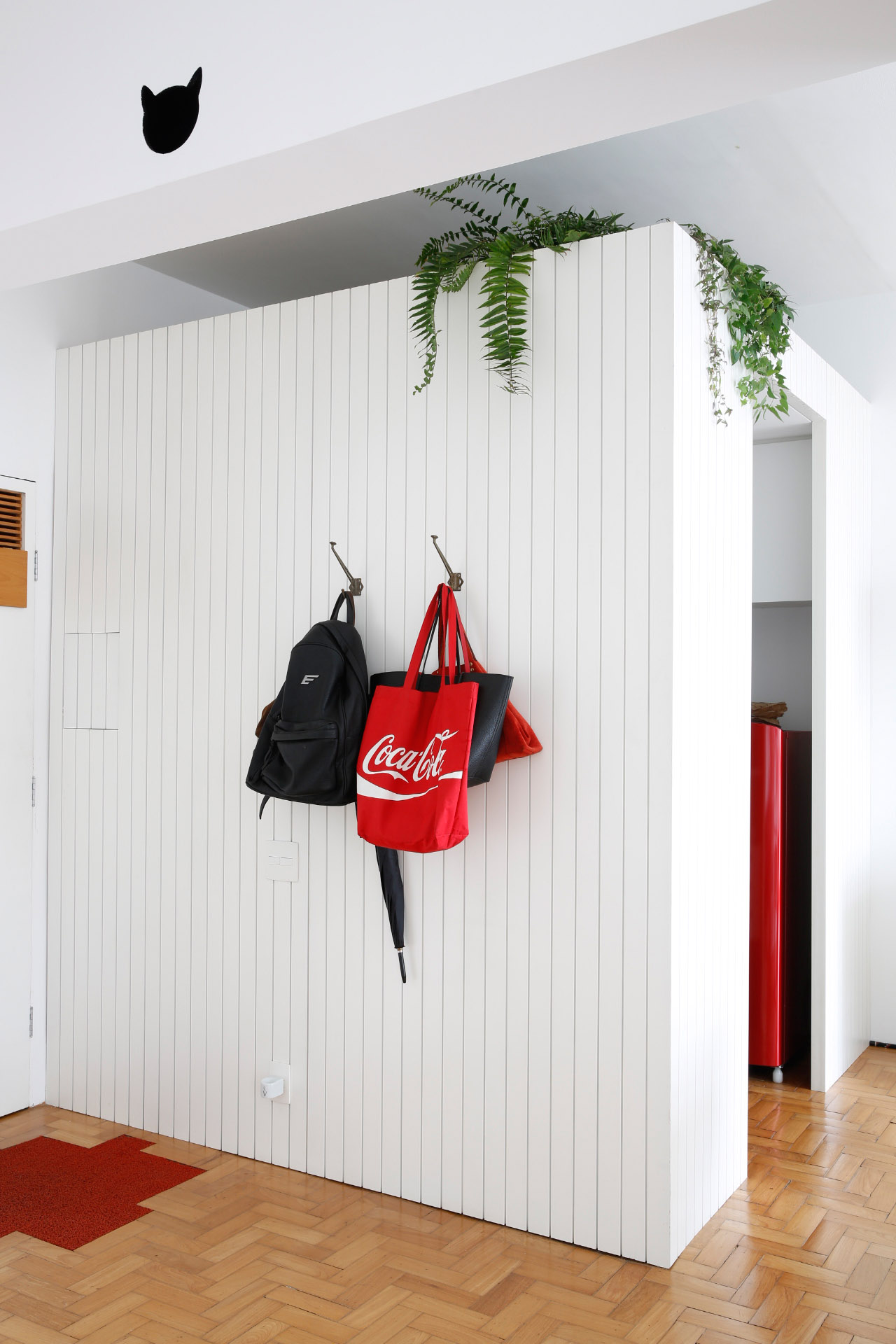 White panelled utility area with hanging bags and trailing plants above, wooden flooring visible.