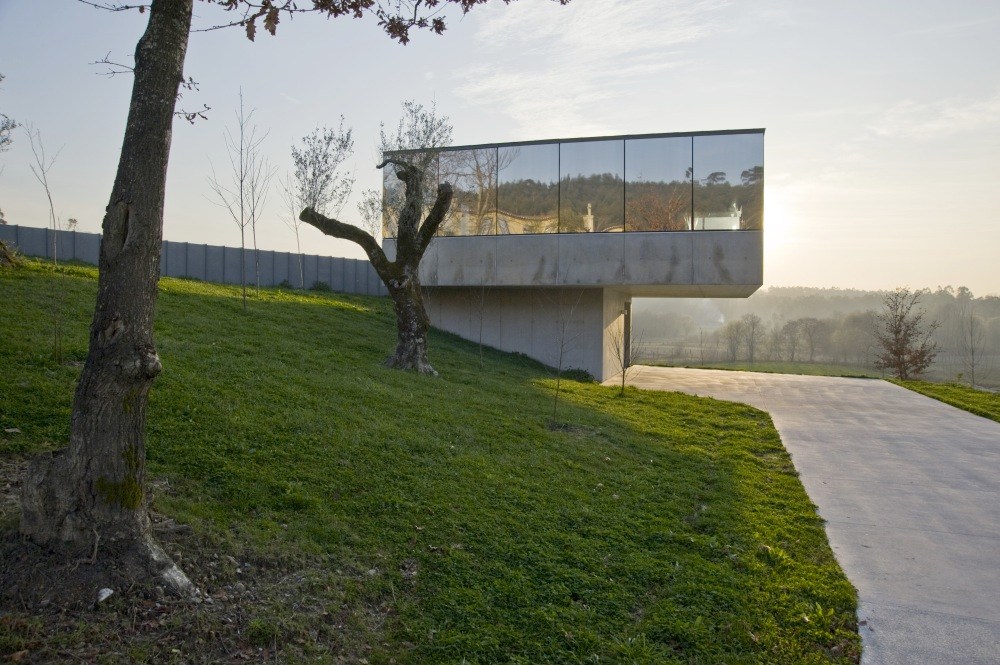 Modern box-shaped house with mirrored glass exterior built on a sloped farm landscape in Portugal.
