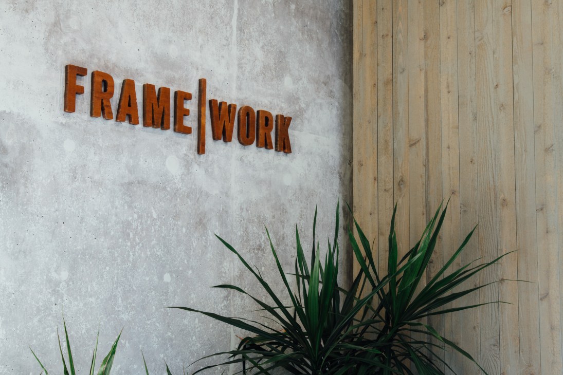 Framework sign in orange letters mounted on concrete wall next to wooden panels and green plant
