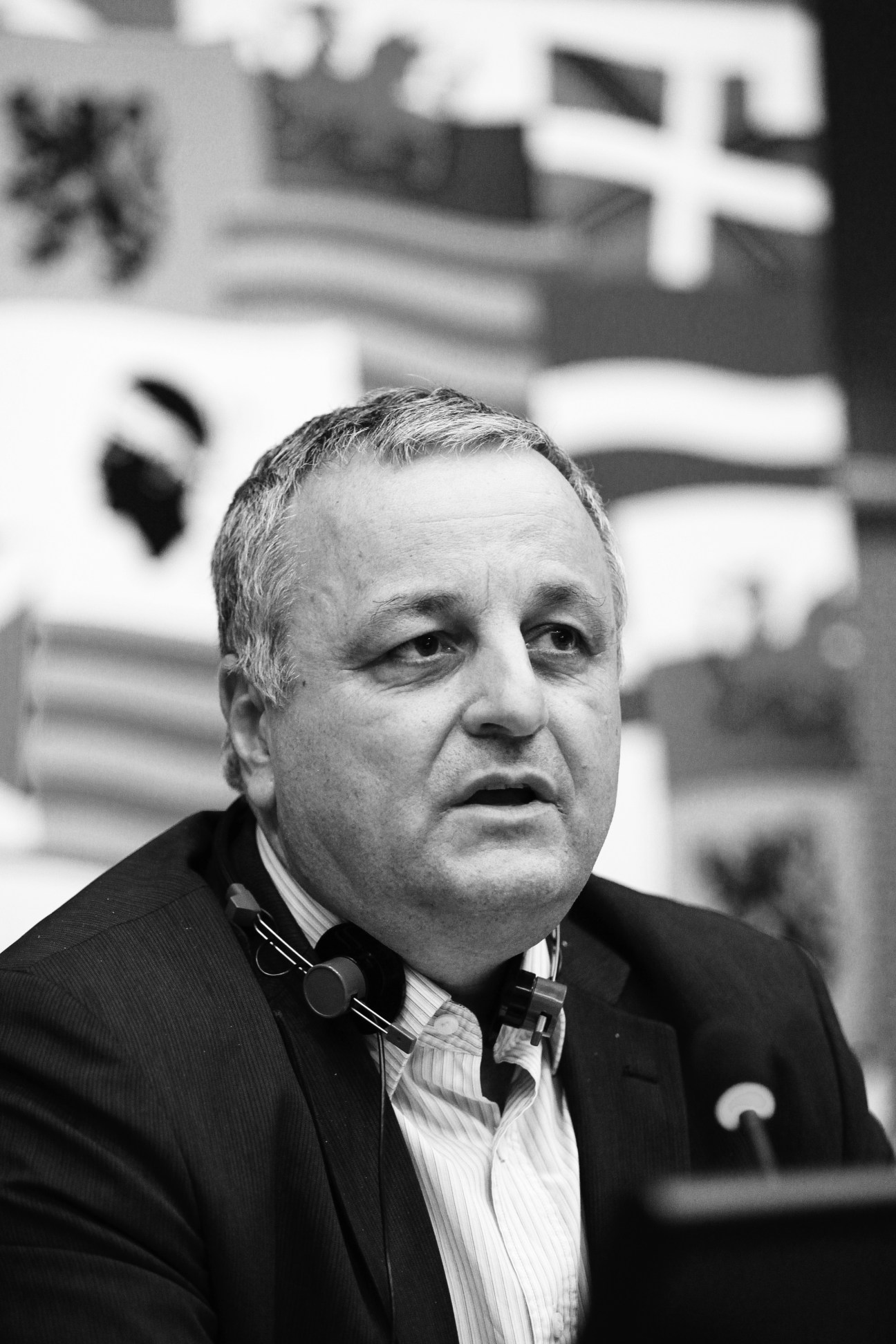 Black and white portrait of François Alfonsi, EU language campaigner, wearing a dark suit and striped shirt at a conference.