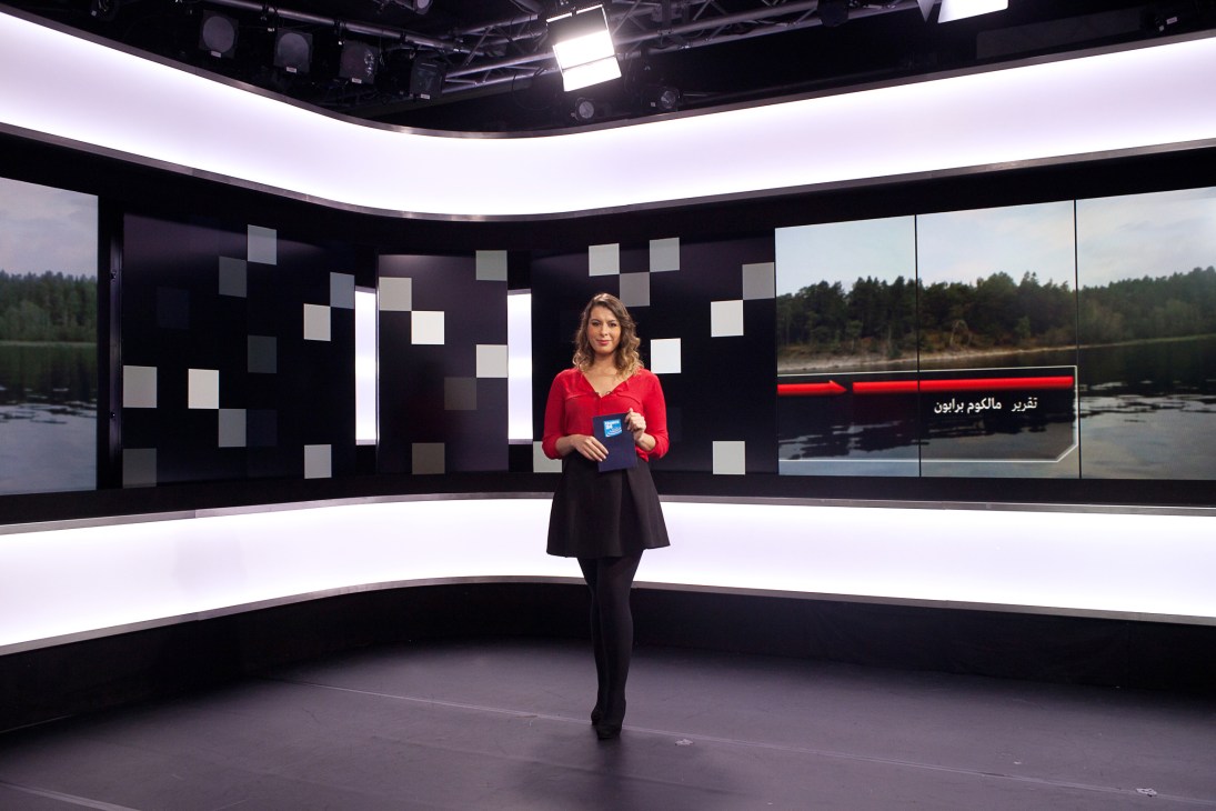 Dounia Nouar presenting in Arabic on the France 24 studio set with video screens behind her.
