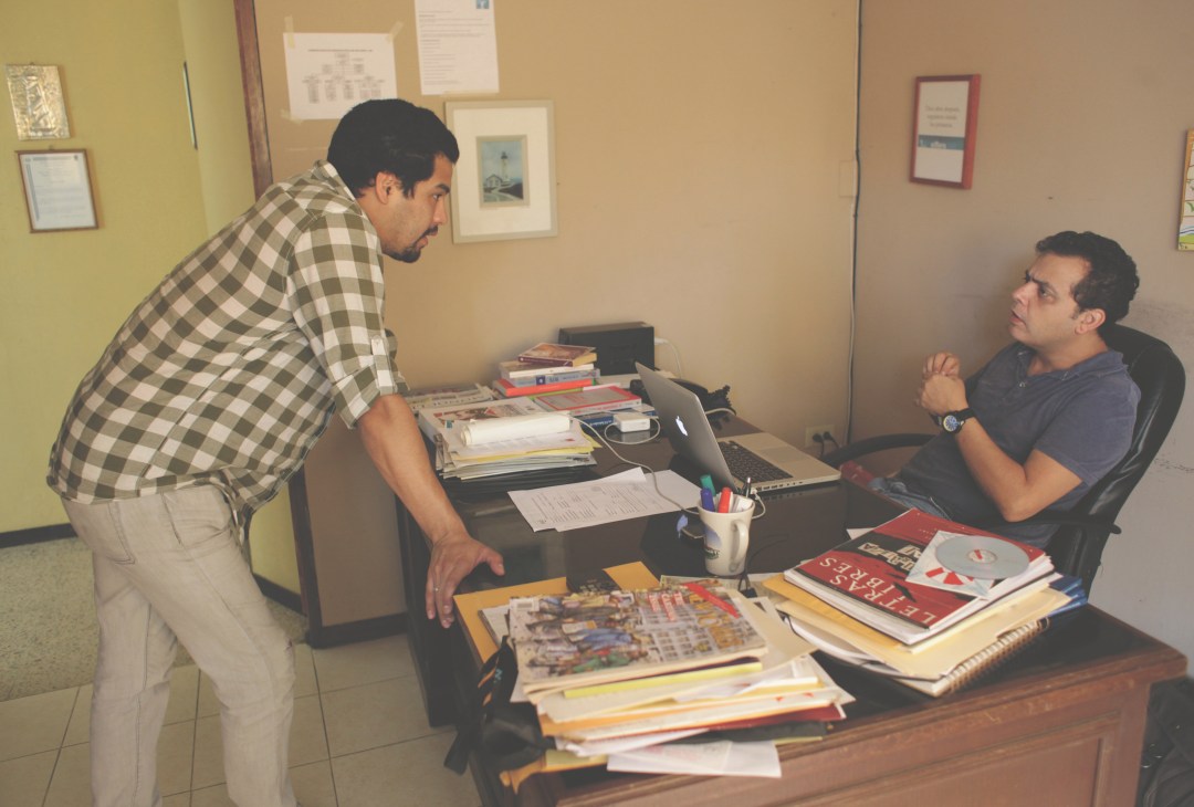Carlos Dada discusses an article about prison violence with journalist Óscar Martínez in an office.