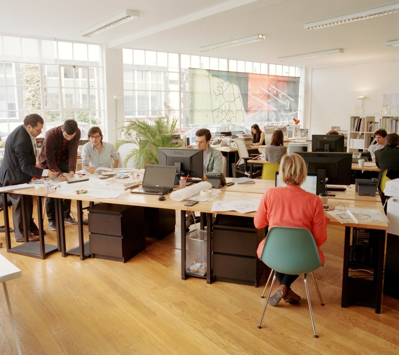 Bright open-plan design studio in Hackney with young architects working at tables and desks near large windows.