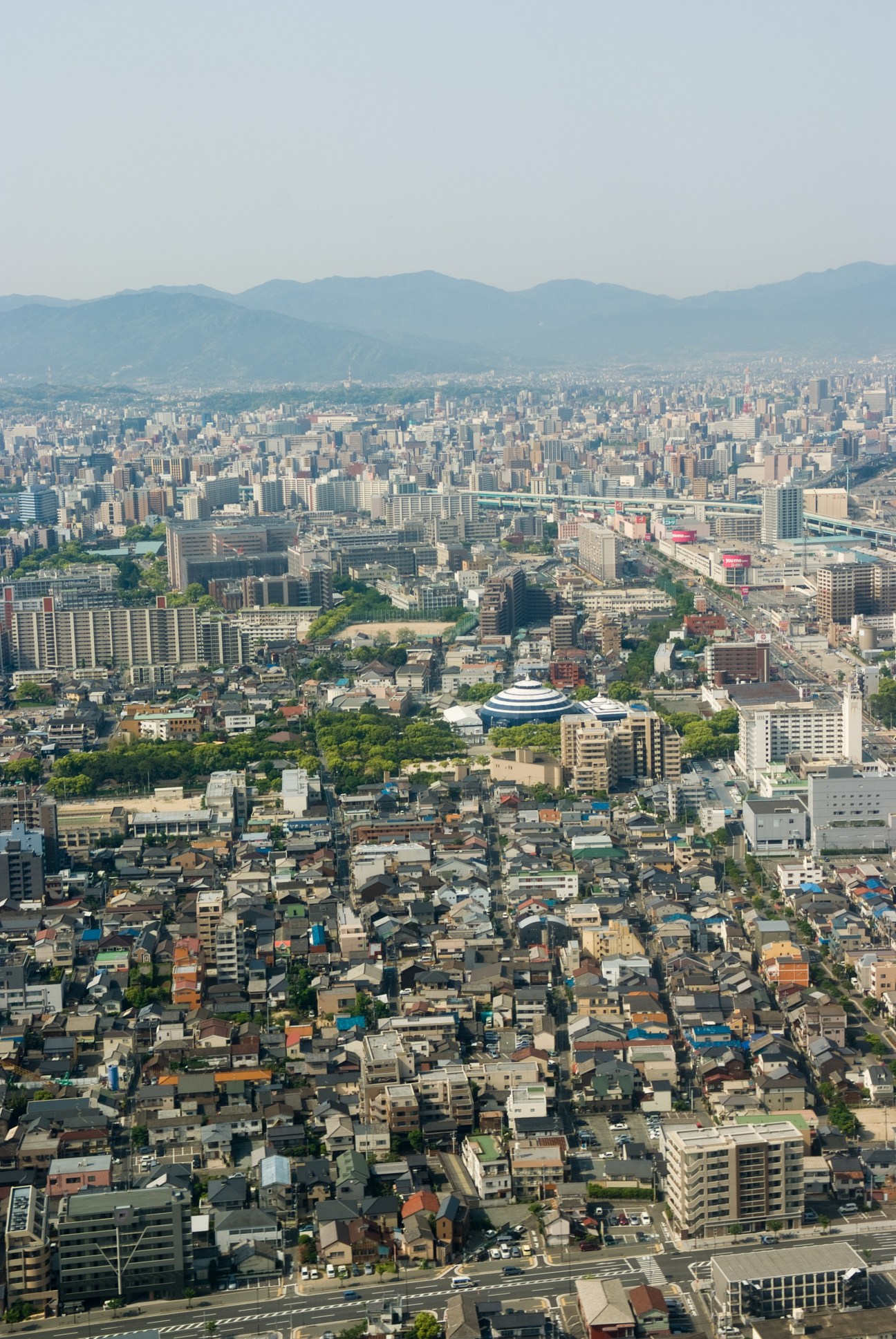 Aerial view of Fukuoka city showing dense urban development with mountains in the distance.