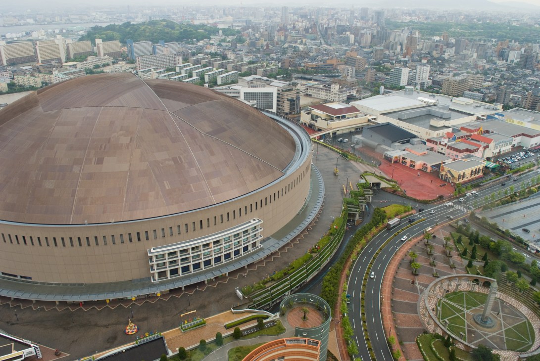 Aerial view of the Fukuoka Yahoo! Japan Dome baseball stadium with the city skyline in the background.