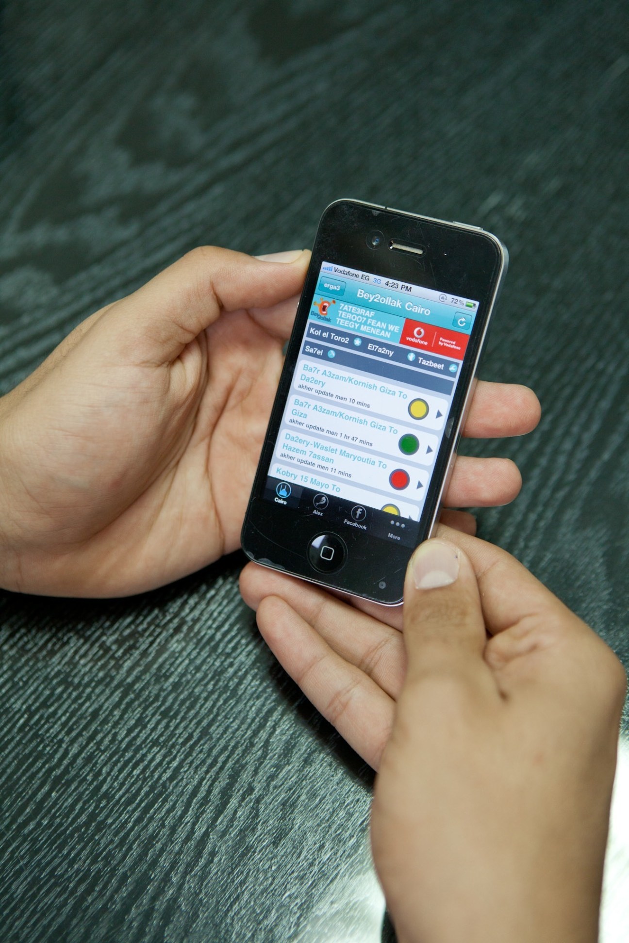 Hands holding an iPhone displaying the Bey2ollak Cairo traffic app with color-coded road status indicators.
