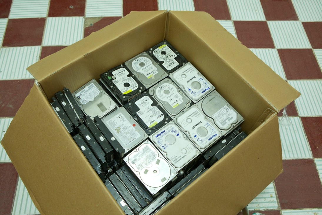 A cardboard box filled with discarded computer hard drives and internal components.