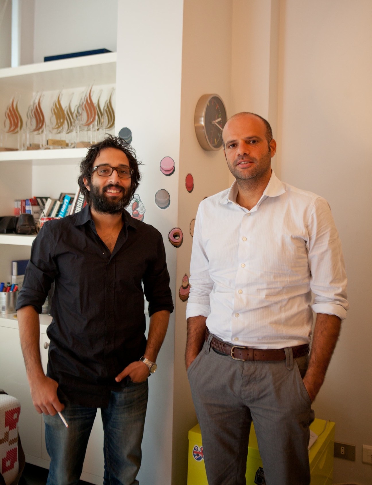Ali Ali and Maged Nassar standing in their office space with shelves and decorative objects visible behind them.