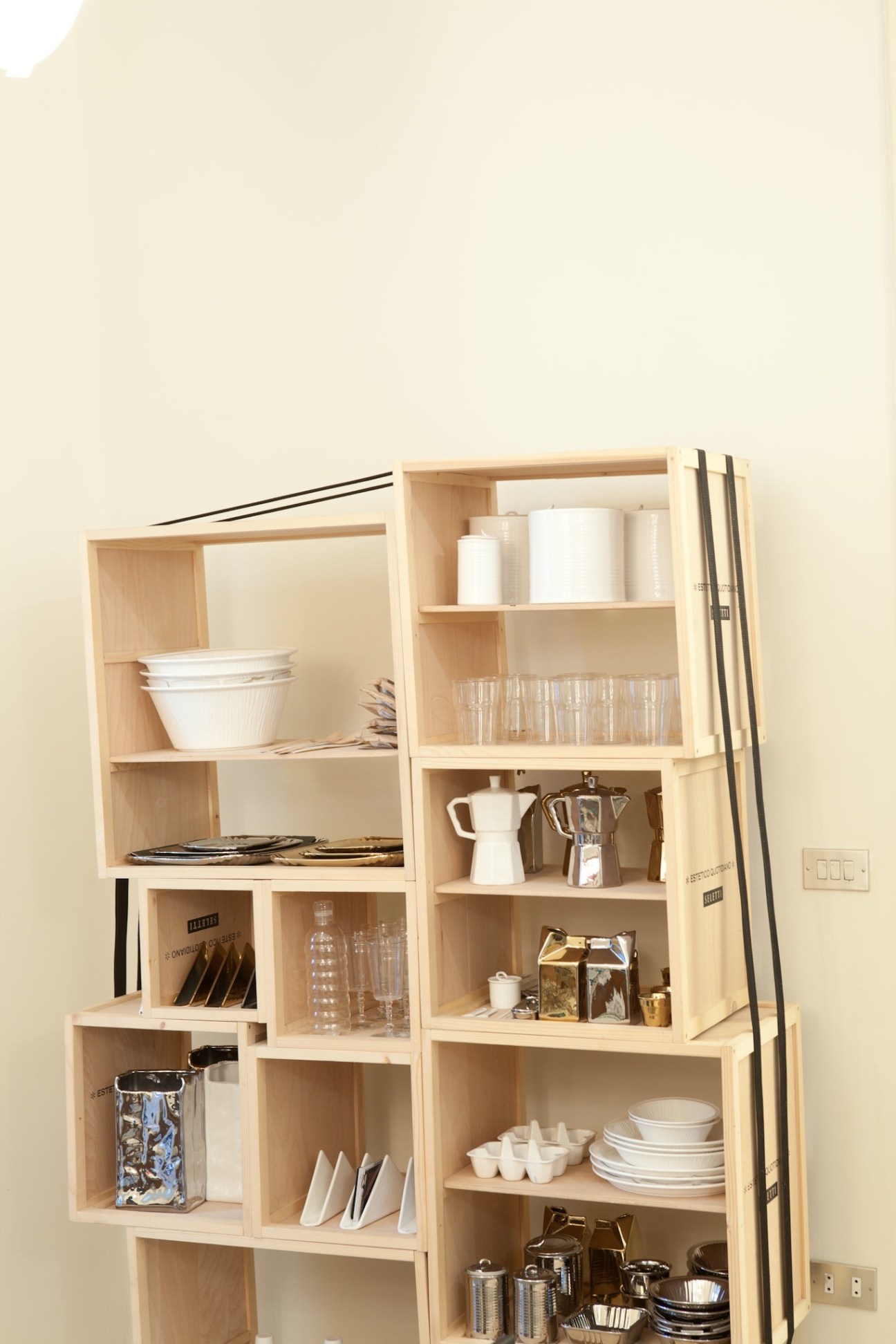 Wooden modular shelving unit displaying kitchen items and tableware against a cream wall.