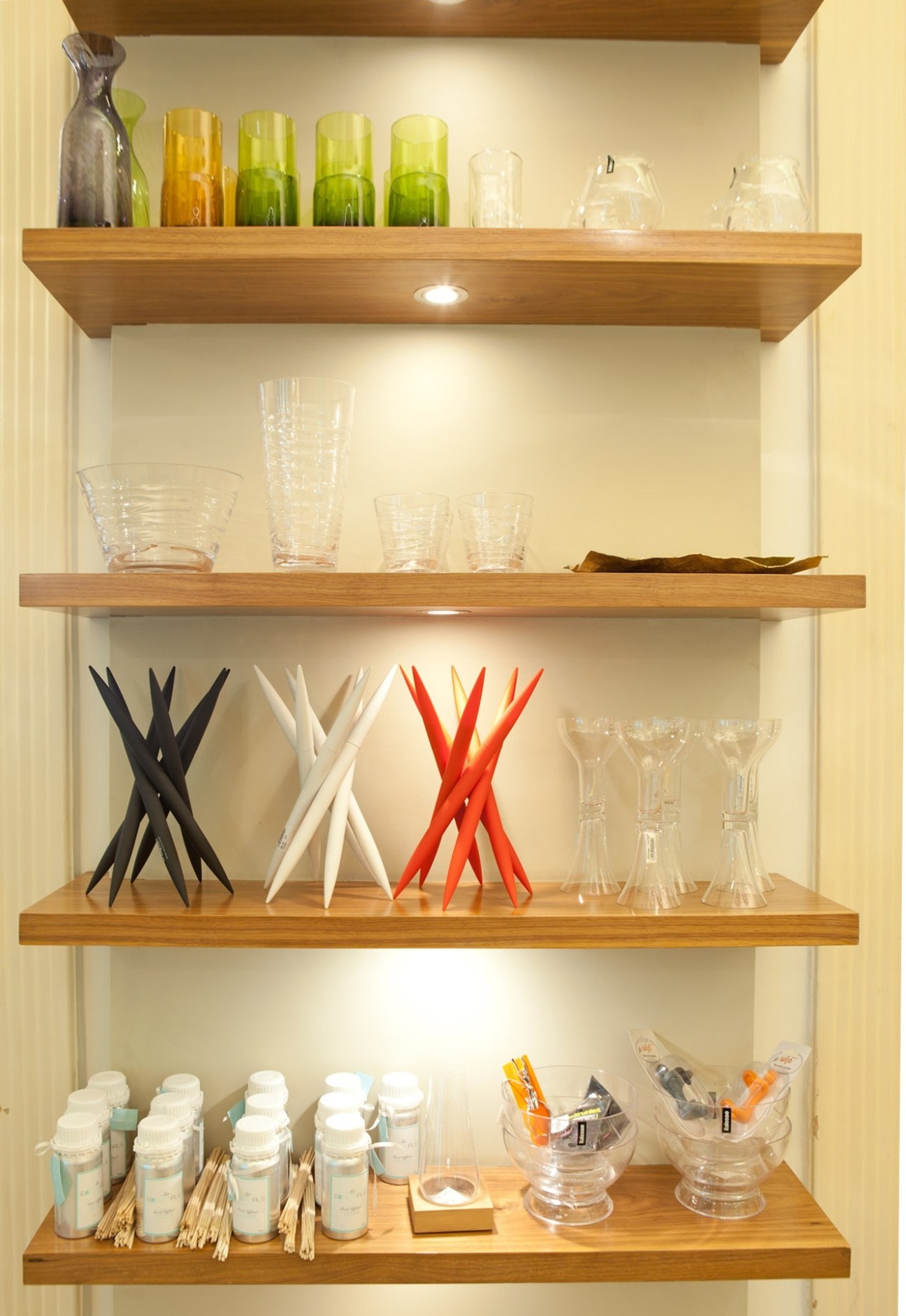 Wooden shelves displaying glassware, colored bottles, decorative objects and tableware.