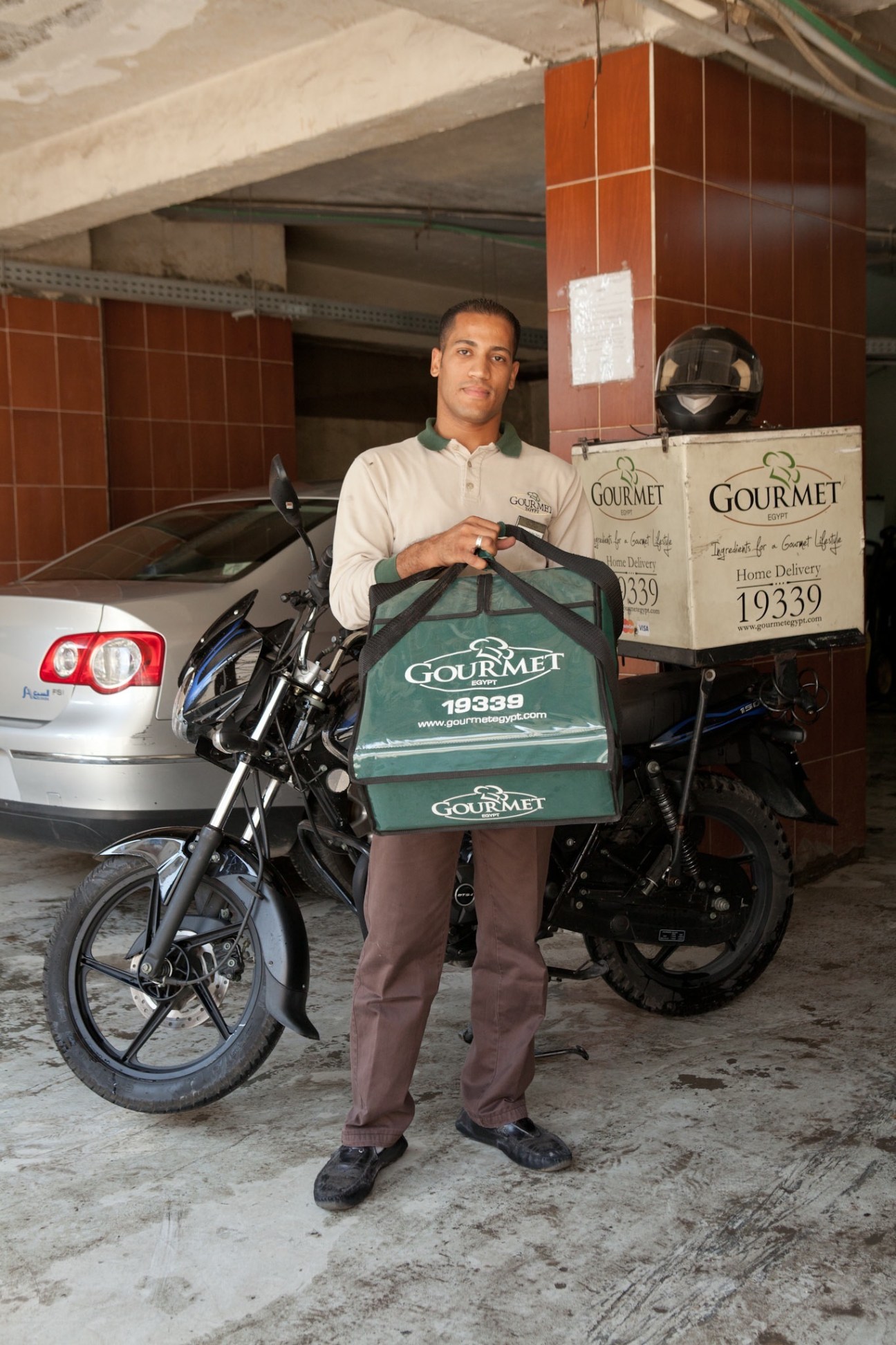 Gourmet Egypt delivery worker holding insulated bag on motorcycle in parking garage