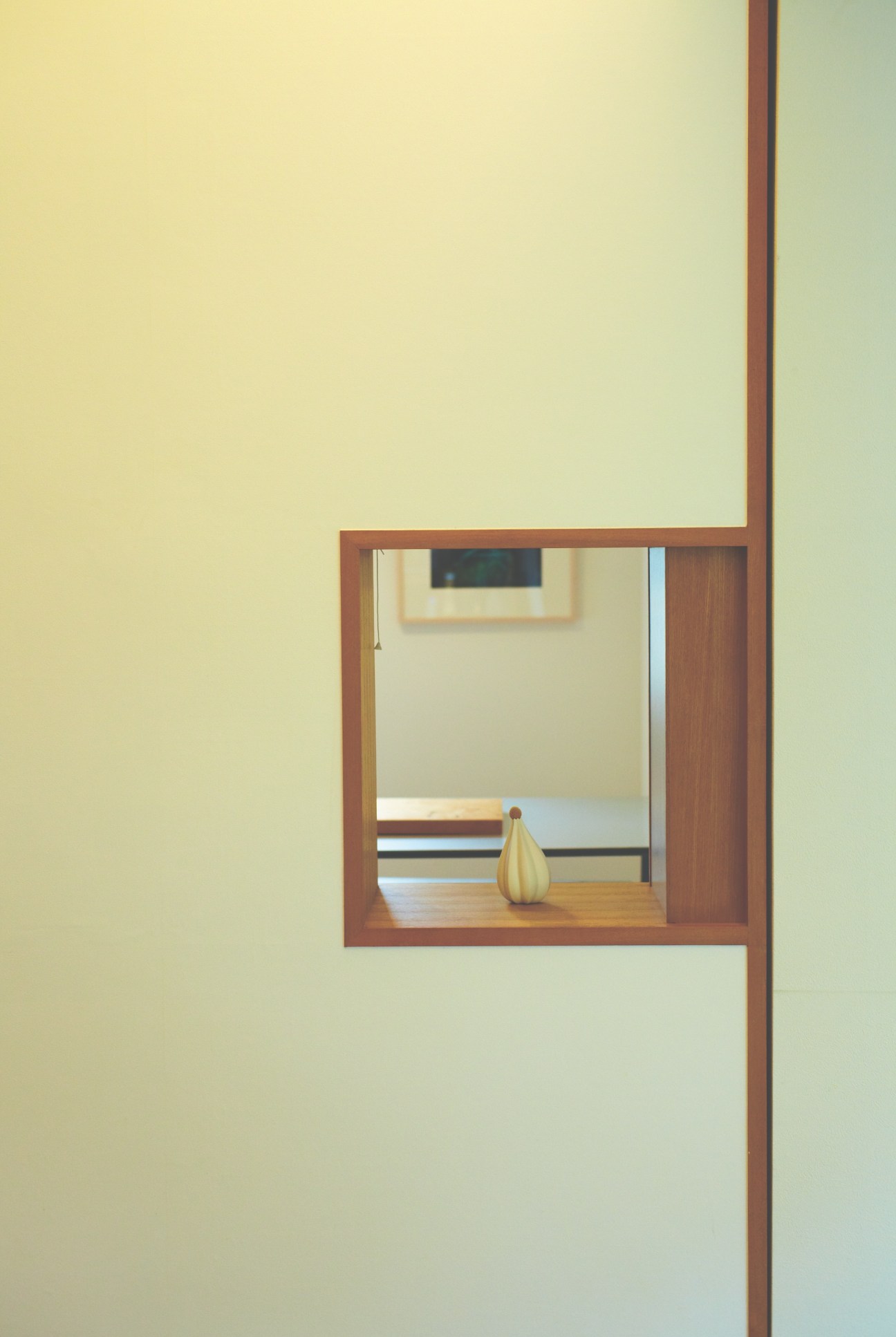 Yellow ceramic vase displayed on wooden shelf in minimalist wooden-framed window alcove.