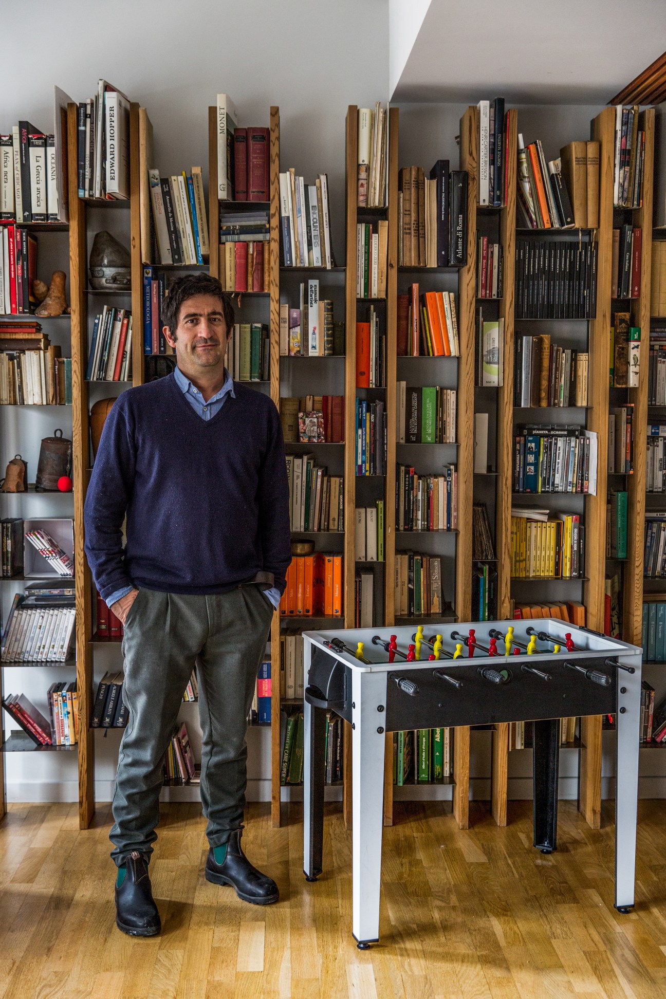 Architect Marco Lanzetta standing in his living room with custom wooden bookshelves and foosball table.