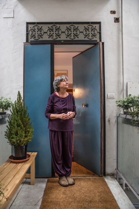 Woman in purple clothing standing at the entrance of a modernist apartment with blue doors and decorative iron railing.