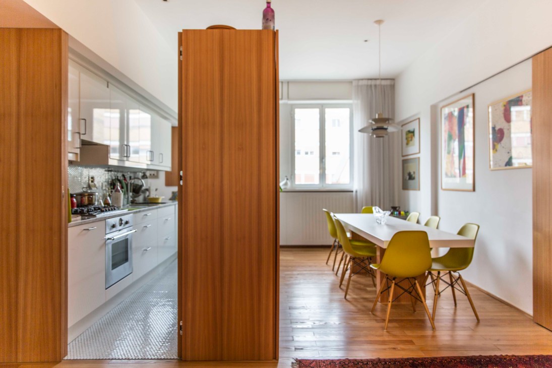 Open-plan kitchen and dining area with wood paneling, white cabinetry, and yellow chairs designed by Marco Lanzetta and Francesca Capitani.