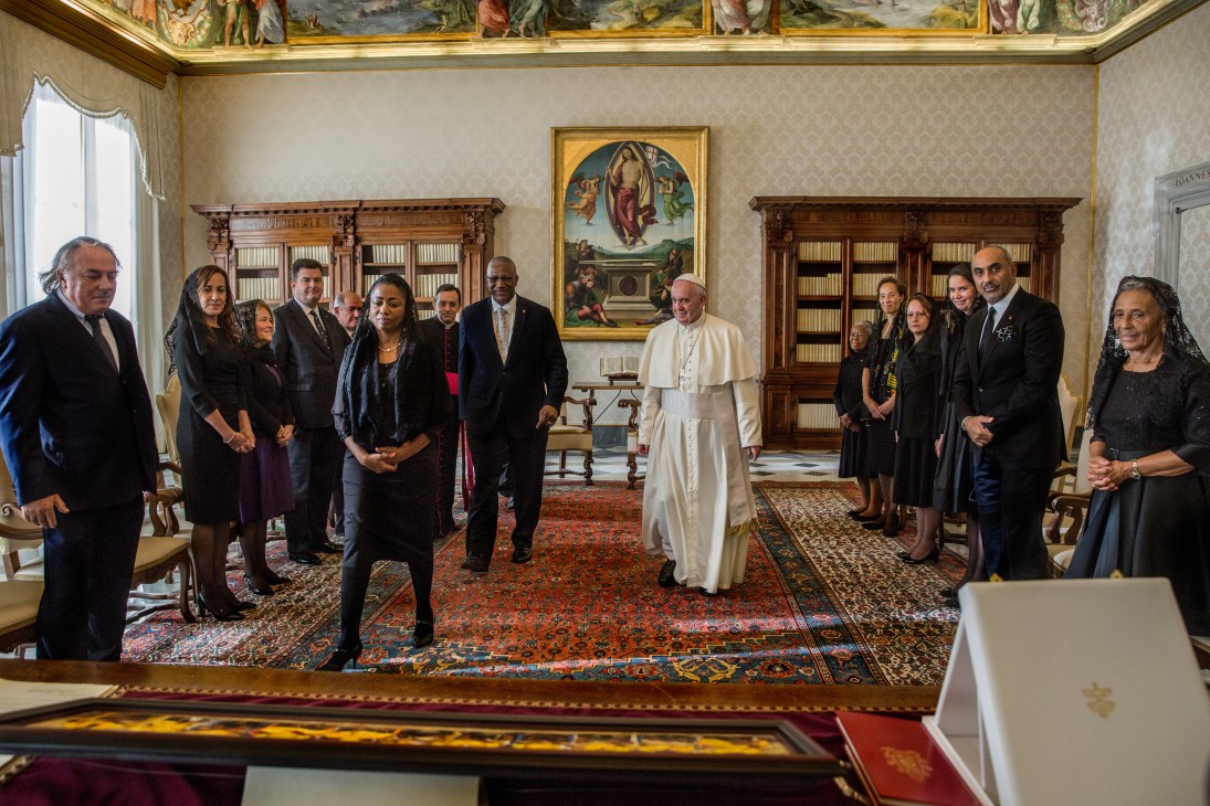 Pope Francis in white robes meets with a delegation from Antigua and Barbuda in an ornate Vatican palace room.