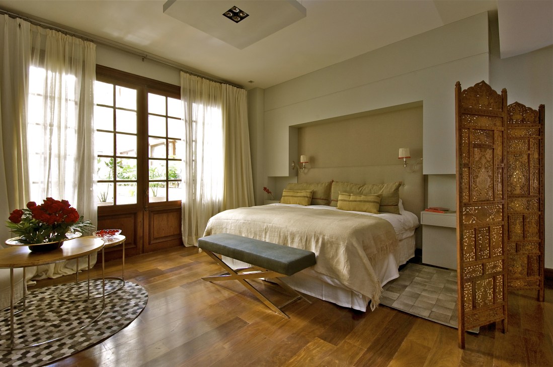 Spacious hotel bedroom with wooden doors, cream curtains, and ornate carved room divider.