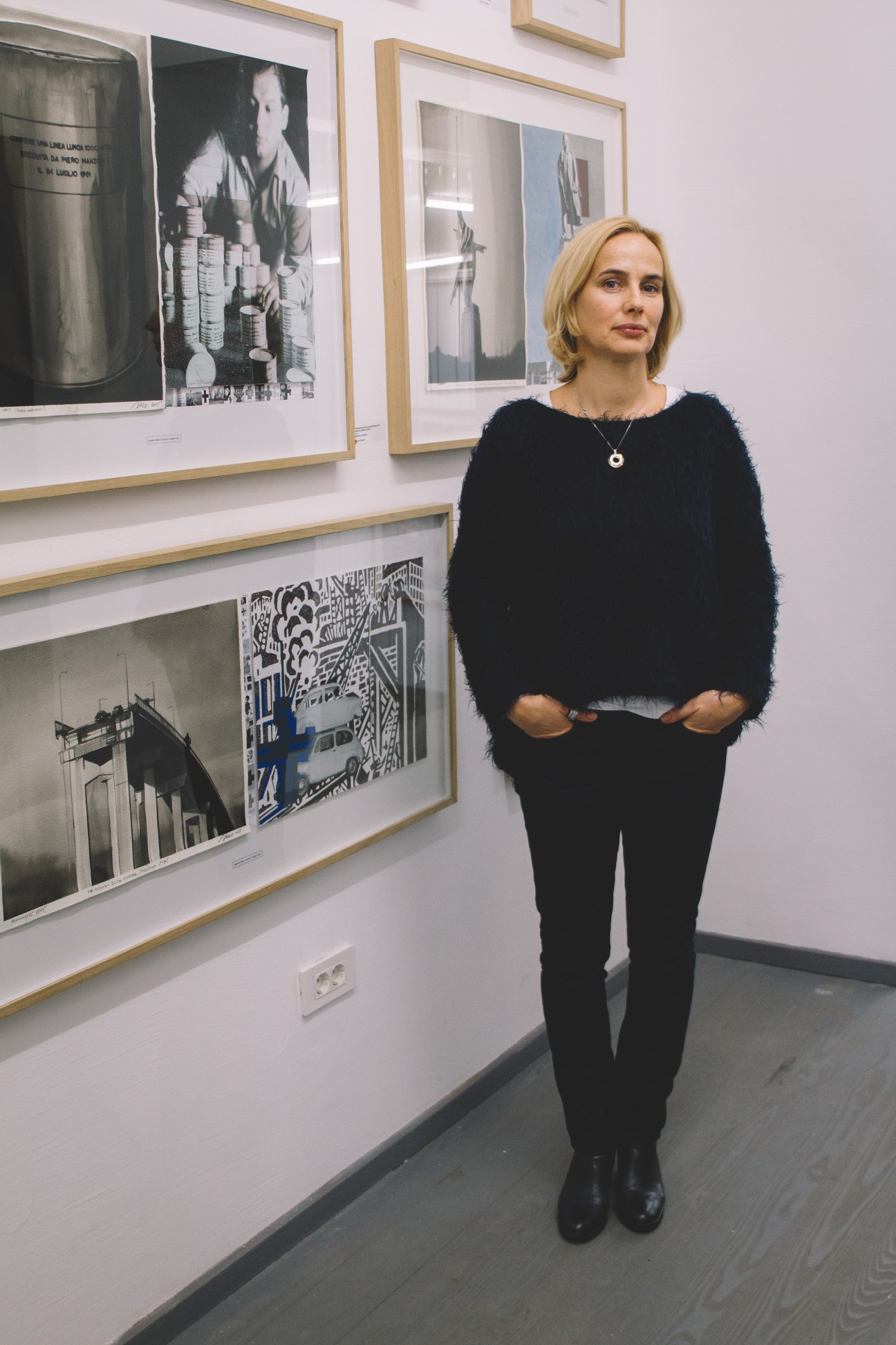 Woman in black sweater standing in gallery with framed black and white photographs on white walls