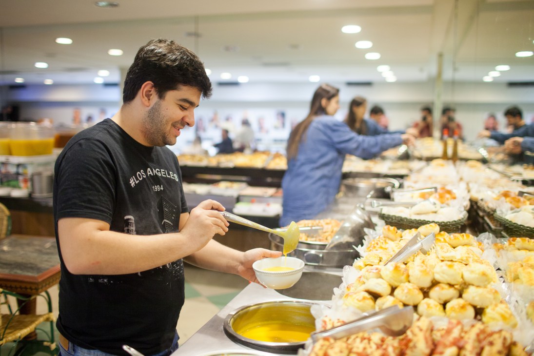 Man in Los Angeles t-shirt serves food from counter at Galeria dos Pães, São Paulo