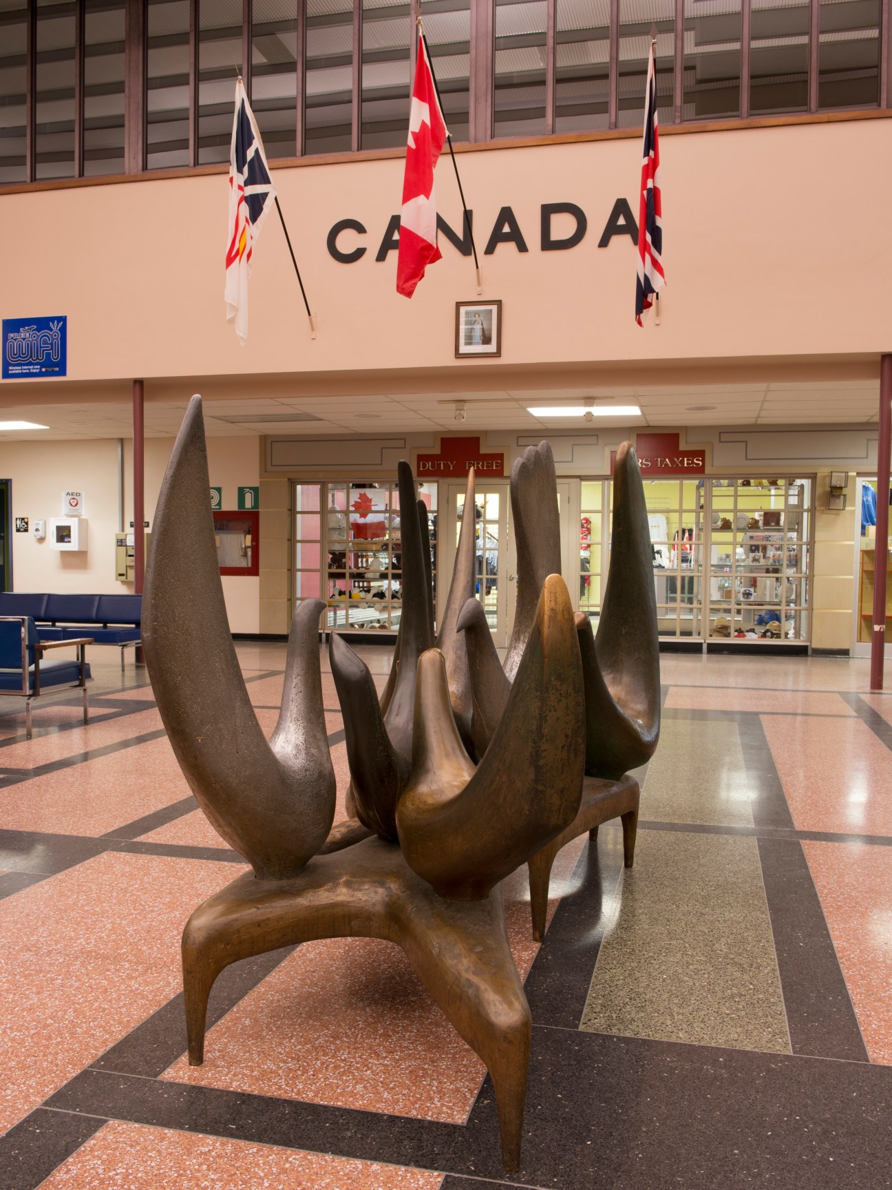Arthur Price's 'Welcoming Birds' bronze sculpture in Gander International Airport terminal with Canadian flags overhead.
