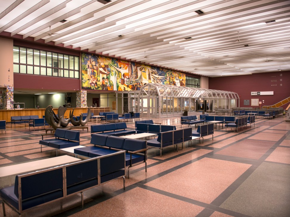 Mid-century modern airport lounge with navy blue seating, colorful mural, bronze sculpture, and geometric terrazzo flooring at Gander International Airport.