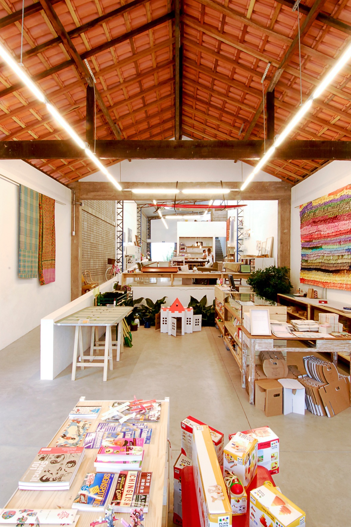 Interior of Amoreira shop in São Paulo showing concrete floors, exposed wooden ceiling beams, and display tables with products.