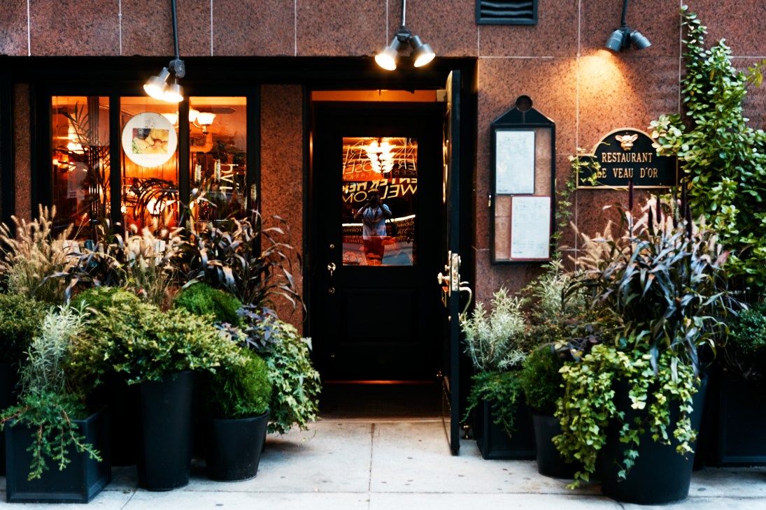 Le Veau d'Or restaurant exterior on East 60th Street with black door, illuminated windows, and planted greenery.