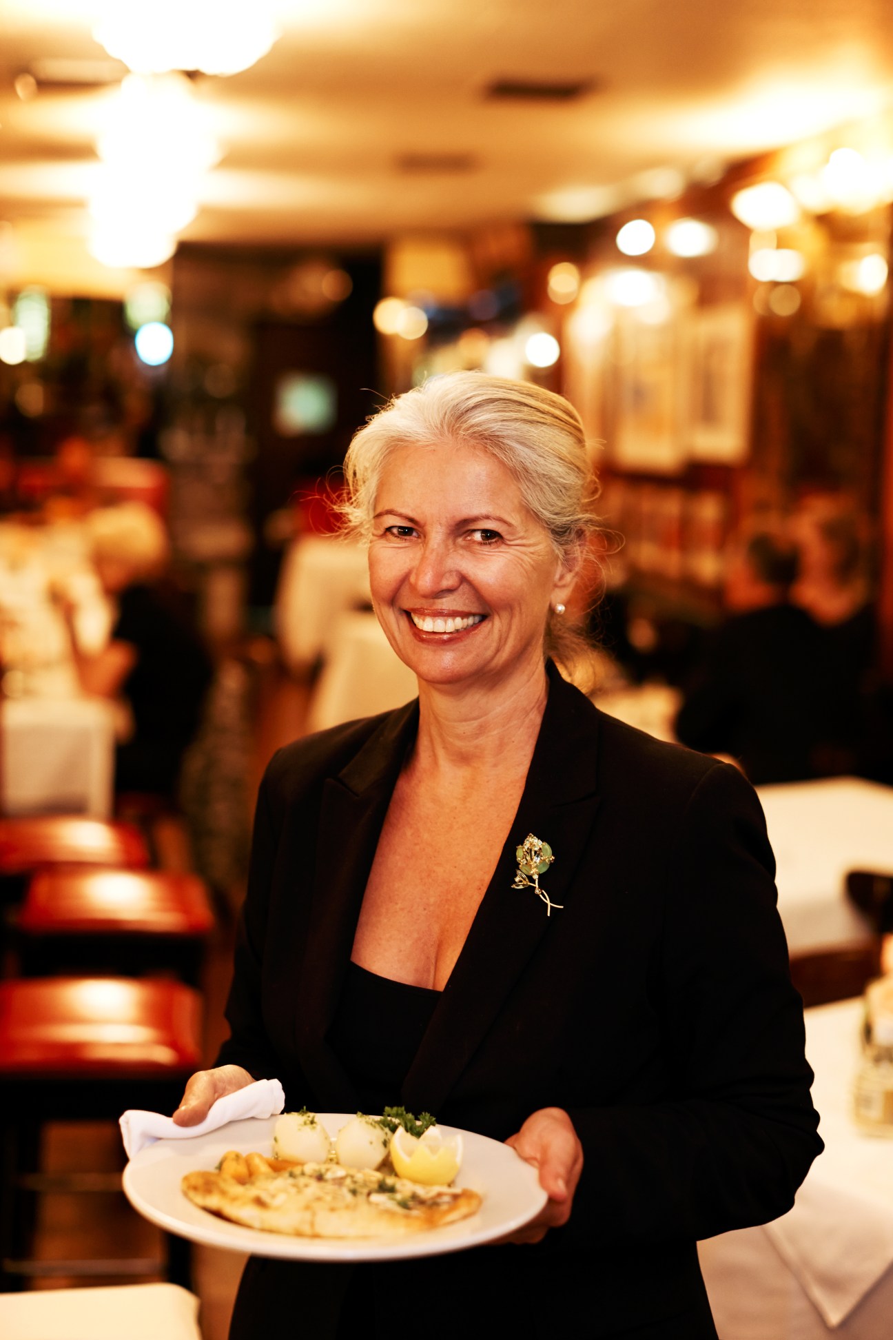 Owner Catherine Treboux smiles while holding a plate of fillet of sole in Le Veau d'Or's dining room.