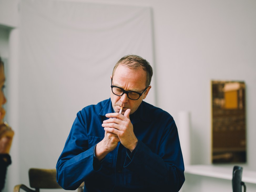 Sculpture professor Heimo Zobernig wearing glasses and a blue shirt, contemplating in his studio.