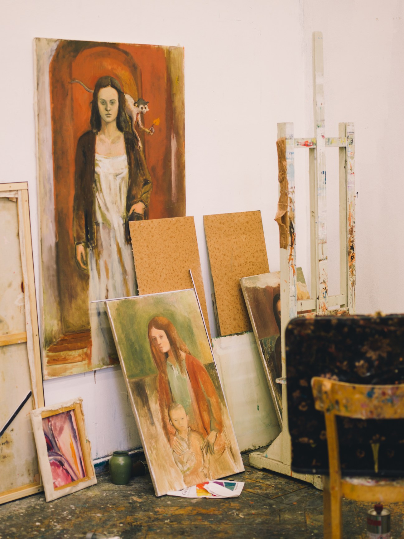 Portrait paintings and canvases lean against white walls in an art studio workspace.