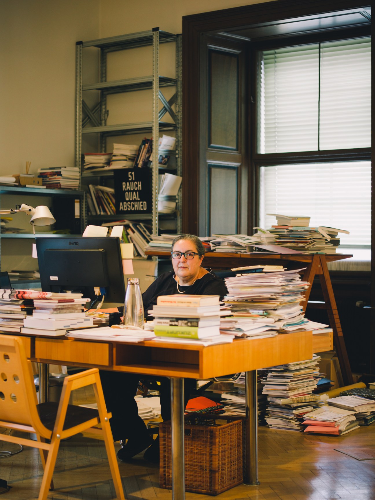 Academy director Eva Blimlinger seated at a wooden desk surrounded by books and papers in a sunlit office.