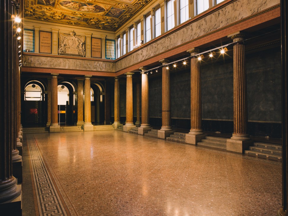 Central auditorium in the Akademie der bildenen Künste with ornate ceiling, classical columns, and polished floor.