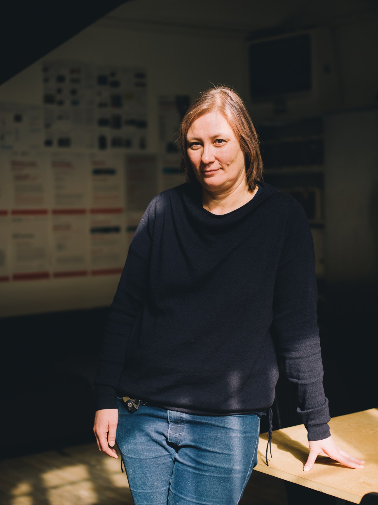 Professor and video artist Dorit Magreiter stands in a studio space wearing a dark sweater and jeans.