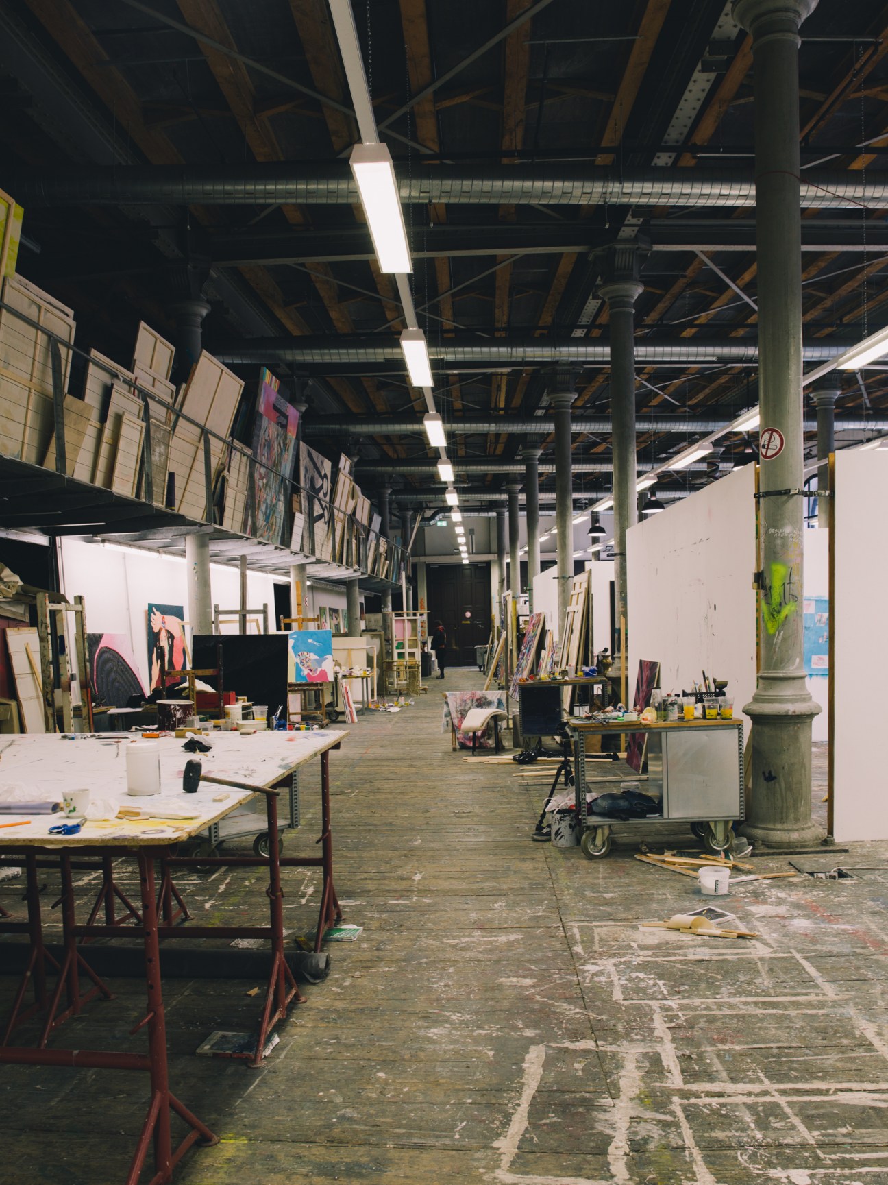 A spacious industrial studio in the Semperdepot with work tables, artwork, and materials under fluorescent lighting.