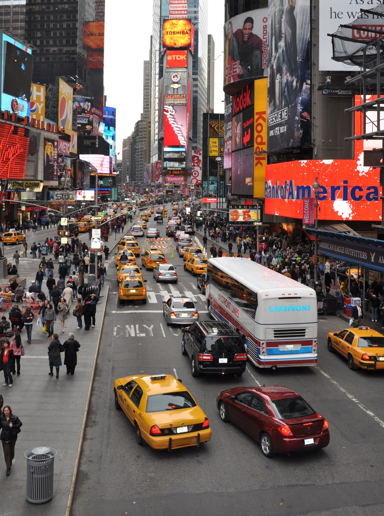 Times Square in New York filled with yellow taxis, cars, buses, and digital billboards with heavy vehicle traffic dominating the street.