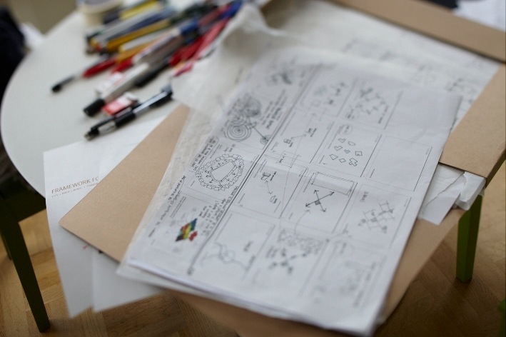 Architectural sketches and city plans laid out on a desk with colored pencils and markers nearby.