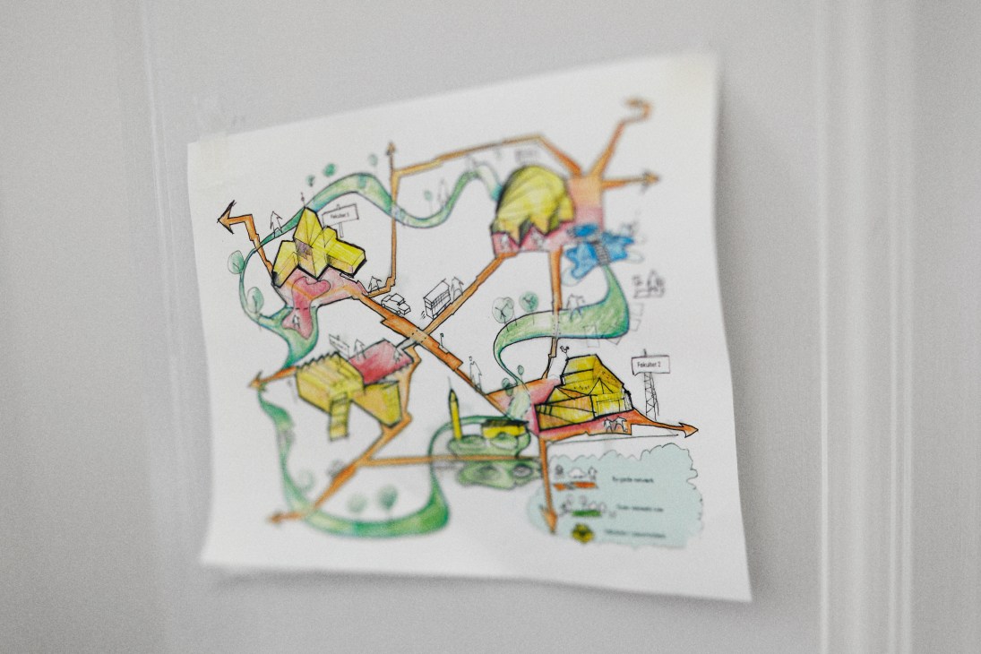 Hand-drawn city planning sketch with colored pencil showing buildings, pathways, and green spaces.